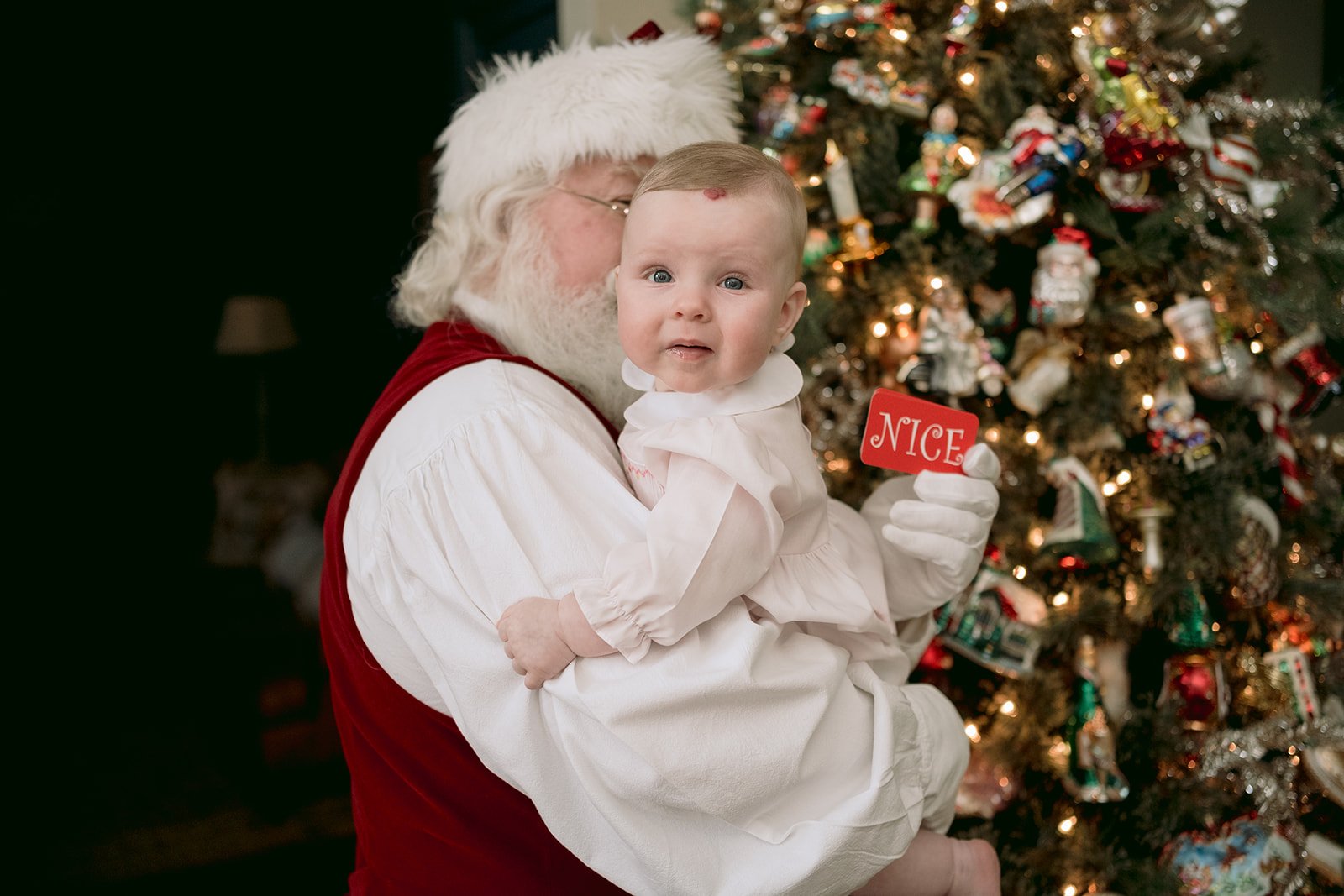 Santa holds young baby girl in from of the Christmas tree.