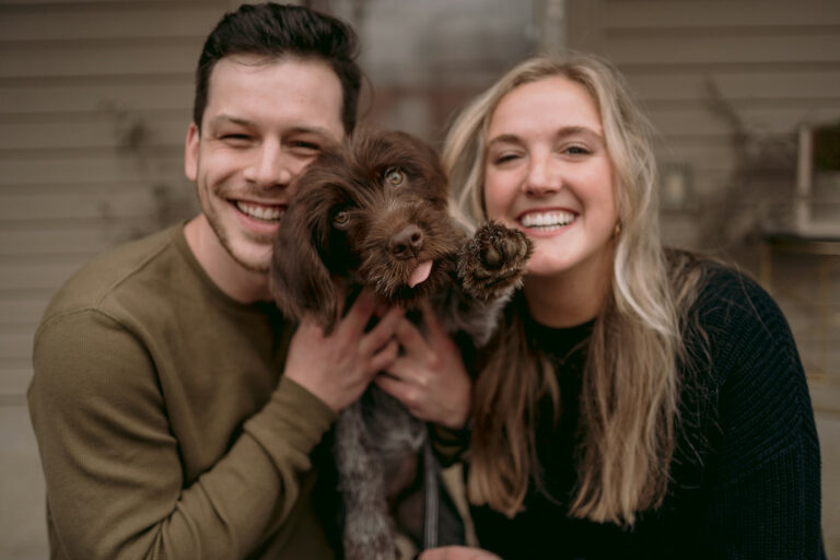 Couple sits on their front porch with their new puppy smiling.