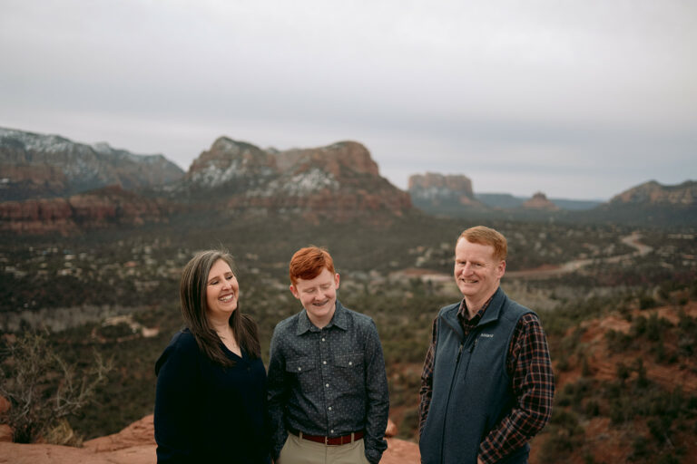 Family stands on top of a mountain at sunrise in Sedona laughing together.