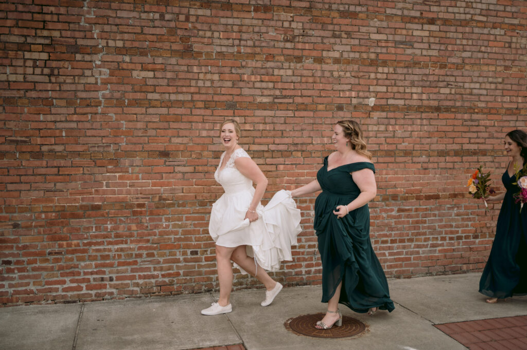 bride holding her dress up and laughing with her bridesmaid while walking