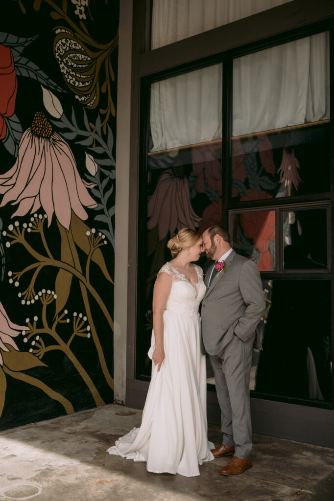 Bride and groom posing together in front of a flower mural