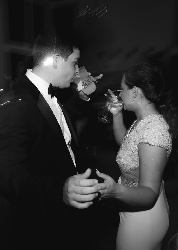 Bride and groom pause dancing to take a drink while holding hands.
